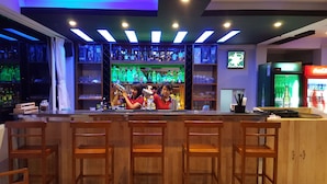 A bar area with wooden bar stools, shelves with bottles, and a neon sign. - Asian Smile Hotel (Yangon)