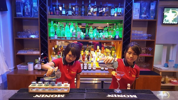 A bar area with a variety of liquor bottles and a bartender preparing a drink. - Asian Smile Hotel (Yangon)