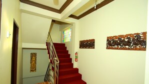 A staircase with red carpeted steps, a metal railing, and a fire extinguisher on the wall. - Hotel Angel Land (Hpa-An)