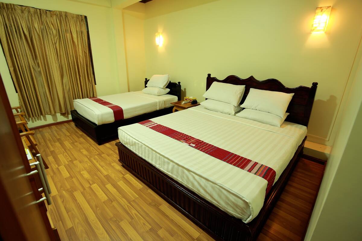 A hotel room with two beds, wooden flooring, and a curtain.