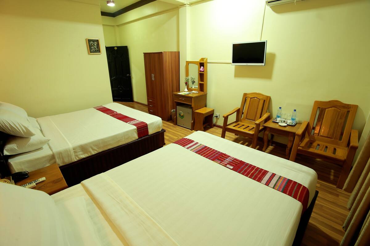 A hotel room with two beds, a desk, a chair, a TV, and a wardrobe.