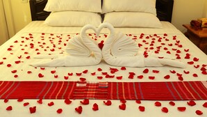A bed with white linens, a heart-shaped towel arrangement, and red rose petals scattered across the bed. - Hotel Angel Land (Hpa-An)