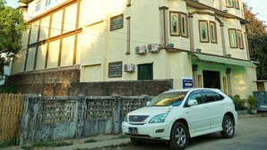 A multi-story hotel with a balcony on the second floor, a sign indicating it is a hotel, and a parked car in front. - Hotel Angel Land (Hpa-An)