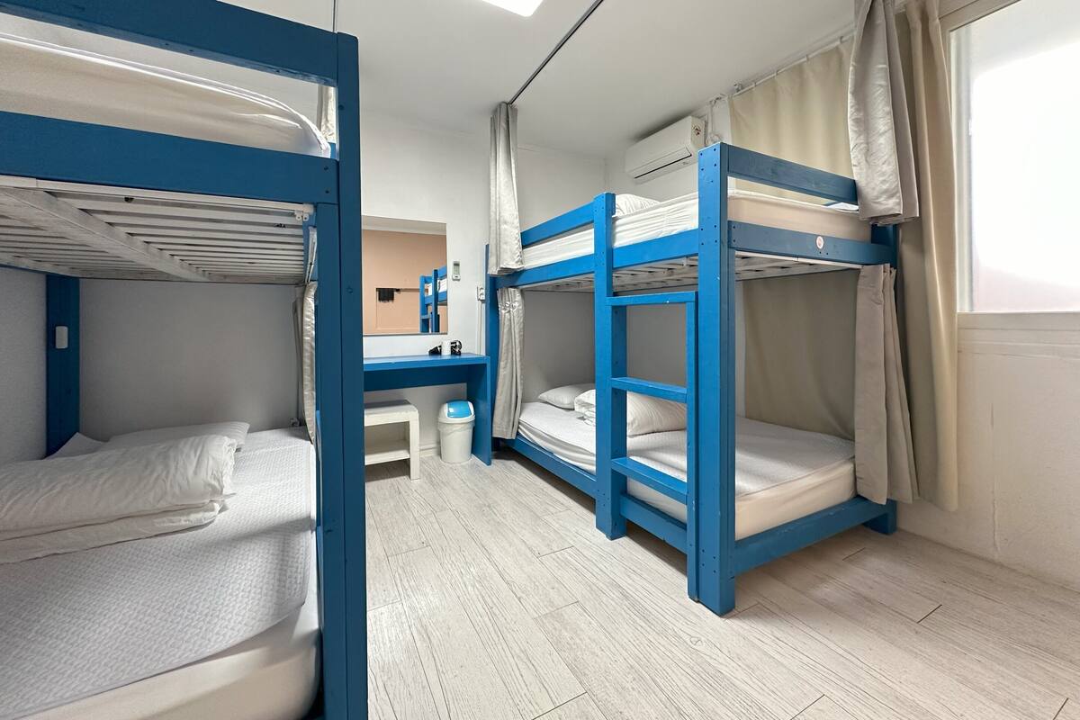 Une chambre de dortoir avec des lits superposés, un bureau et une fenêtre avec des rideaux.