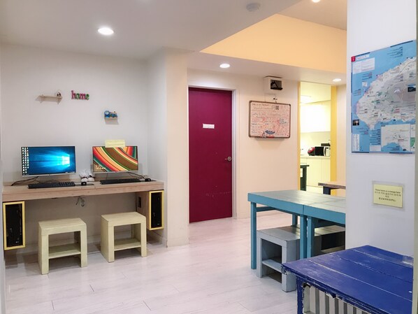 Een kamer met een bureau, twee monitoren, een rode deur, een whiteboard en een kaart aan de muur.