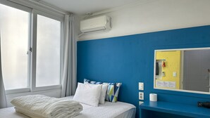 Et hotelværelse med en seng, et vindue med gardiner, et klimaanlæg, et spejl og en blå væg.