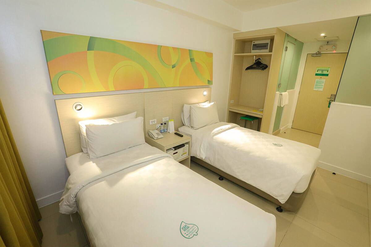 Une chambre d’hôtel avec deux lits, une grande peinture abstraite au mur, une table de chevet avec une lampe et un miroir.