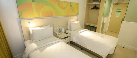 A hotel room with two beds, a large abstract painting on the wall, a bedside table with a lamp, and a mirror.
