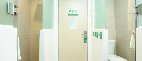 Un baño con ducha, inodoro y una puerta con panel de control.