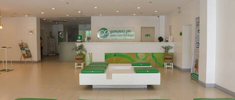 A reception area with a white reception desk, green cushioned seating, and a sign for Go Hotels Manila Airport Road.