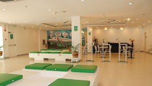 Eine moderne Hotelhalle mit grünen Sitzbereichen, einem Empfangstresen und einem Wandgemälde.