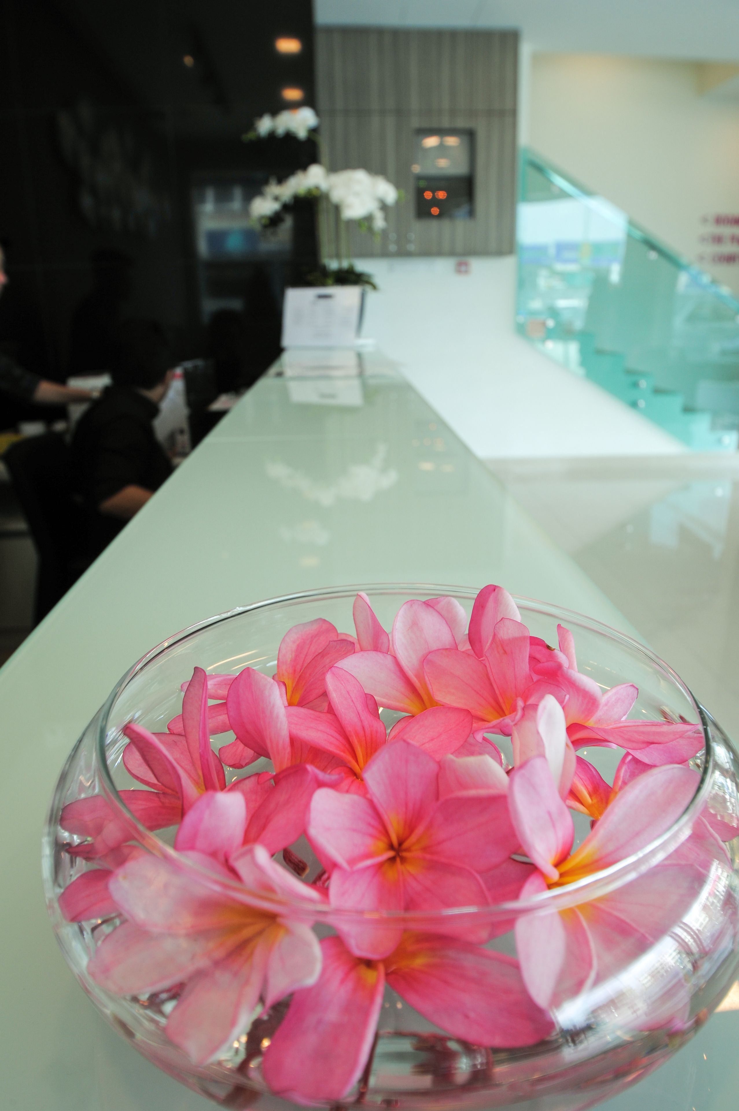 Uma área de recepção com uma mesa de vidro exibindo flores cor-de-rosa.