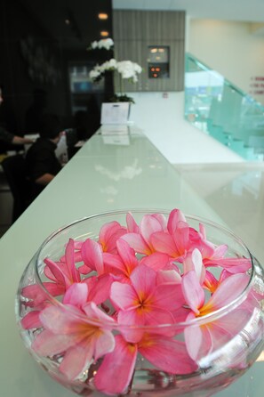Un espace d’accueil avec une table à plateau de verre sur laquelle sont disposées des fleurs roses.