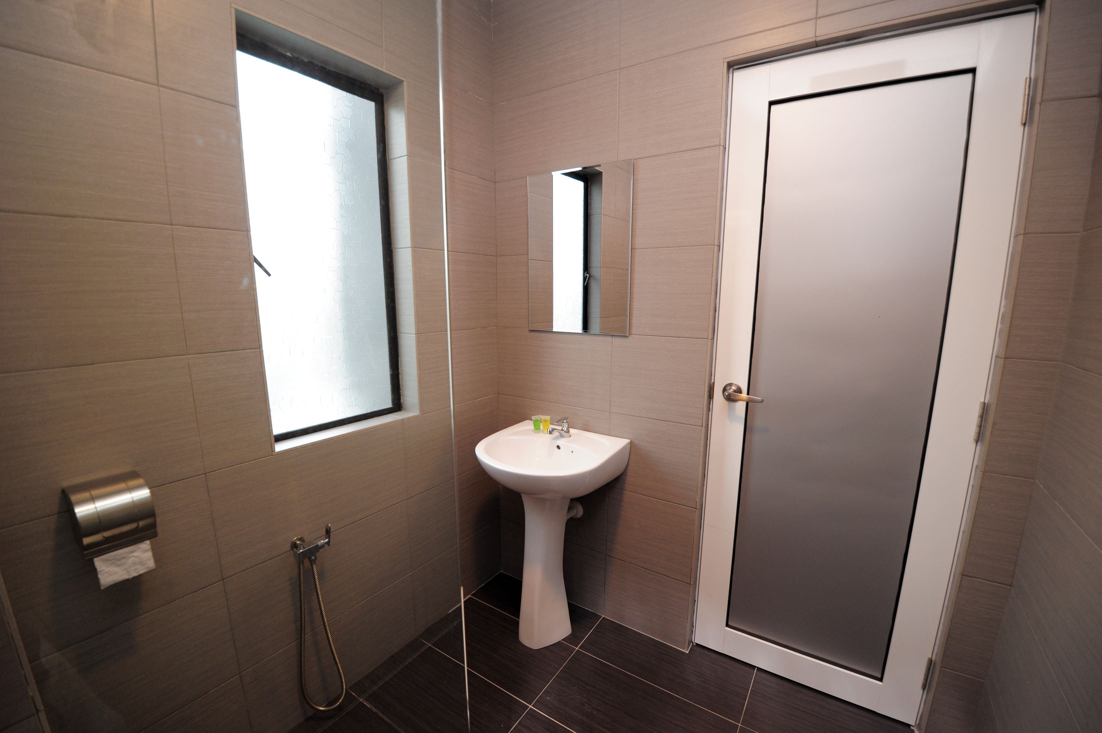 A bathroom with a sink, mirror, toilet paper dispenser, and a shower.