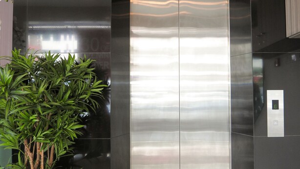 A modern elevator with a metallic finish, flanked by black walls and a potted plant. - Hotel Mezzo (Kuala Lumpur)