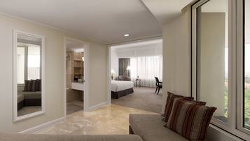 A hotel room with a large bed, a sitting area with a sofa, a small table, and a large window offering a view.