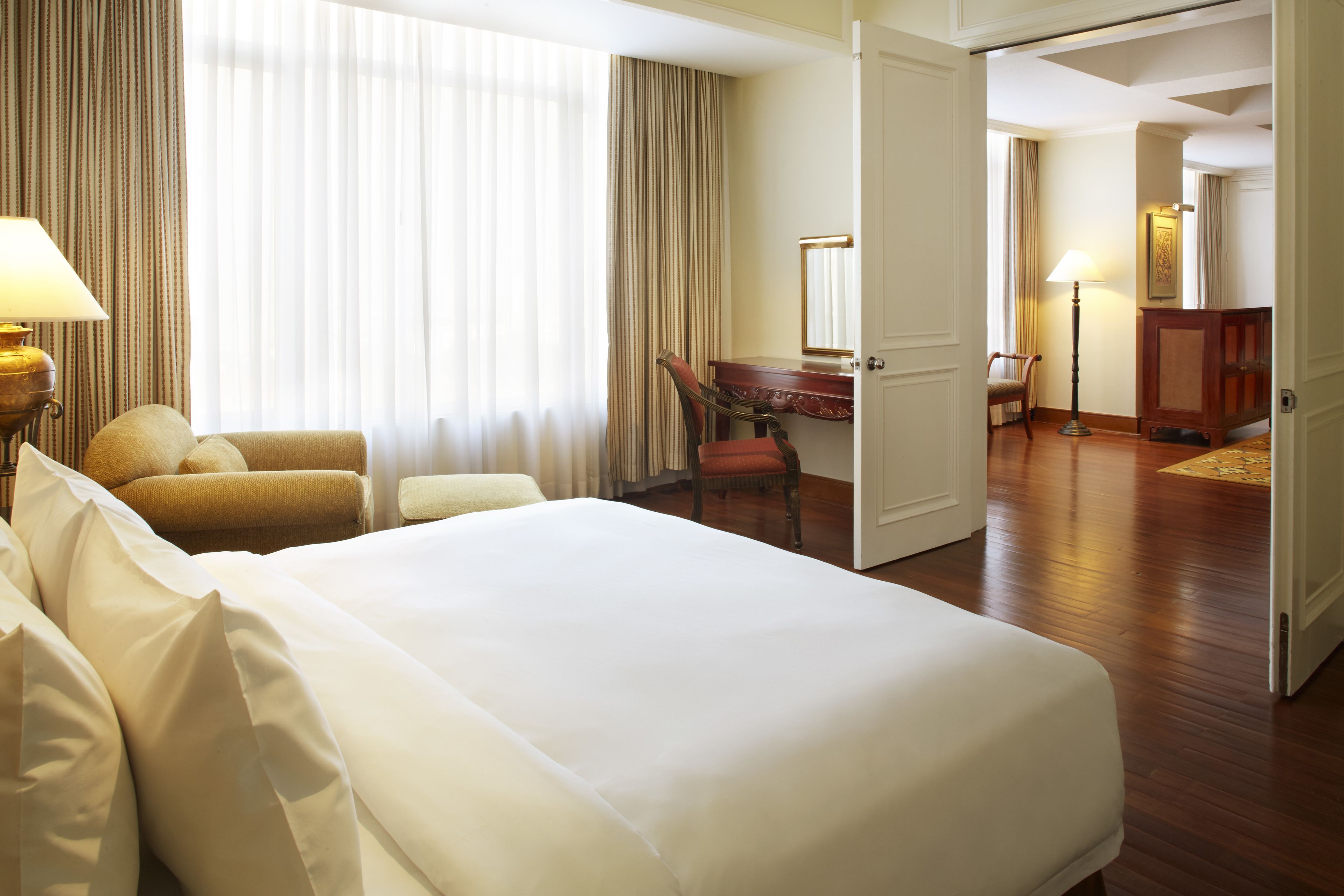 A hotel room with a large bed, a desk, a chair, and a lamp.