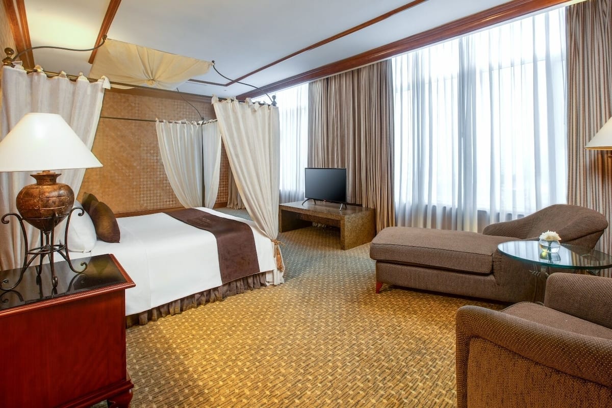 A hotel room with a bed, a TV, a desk, a chair, and a small table with a vase.