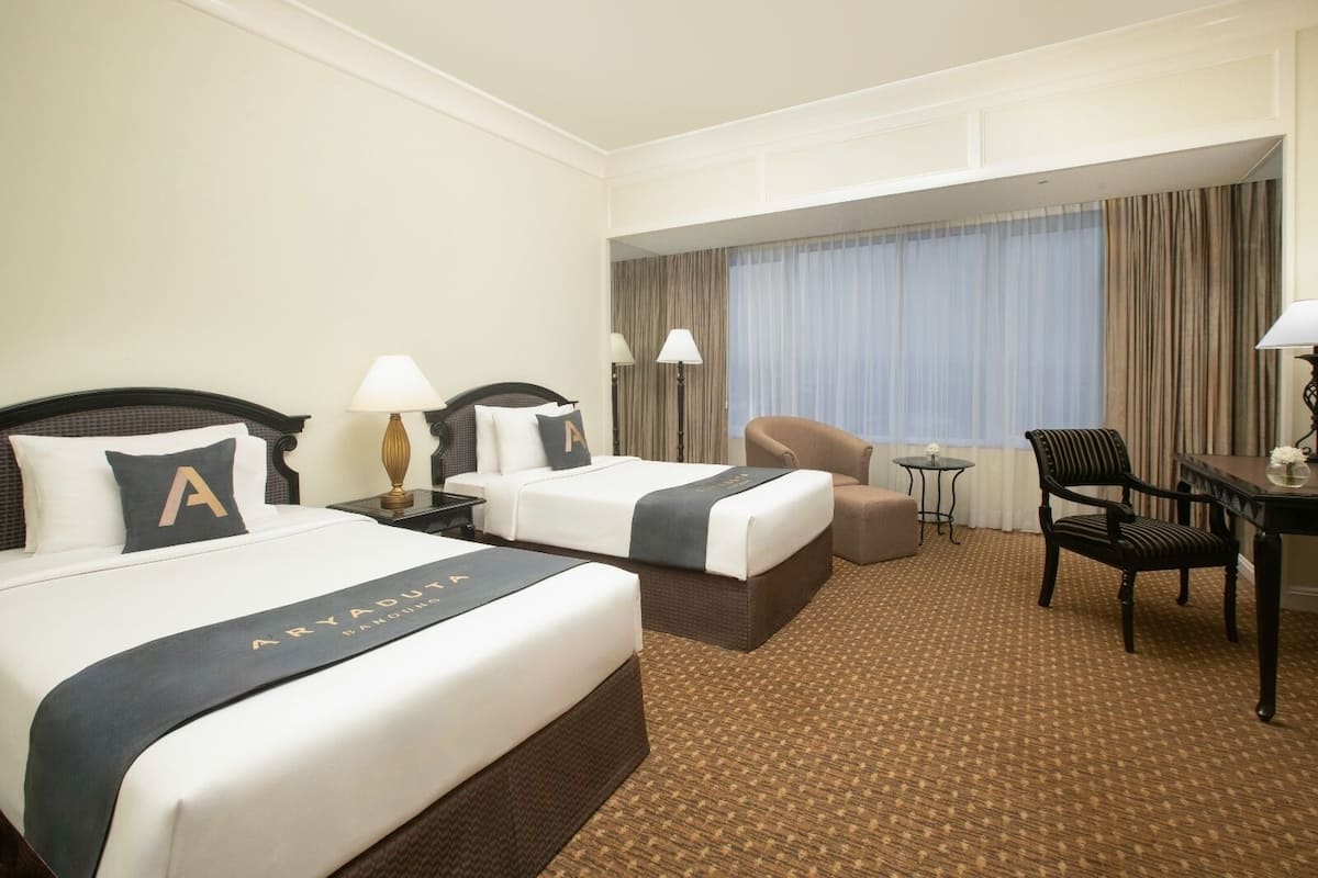 A hotel room with two beds, a desk, a chair, and a small table.