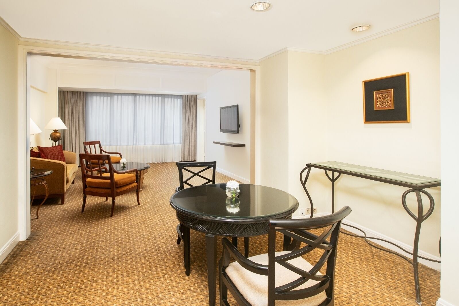 Habitación de hotel con una mesa de comedor redonda, dos sillas, un sofá, una lámpara y un televisor en la pared.