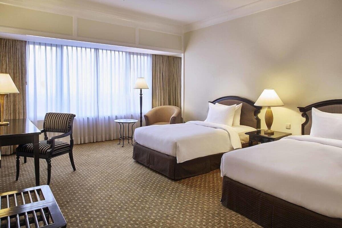 A hotel room with two beds, a desk, a chair, and a small table.