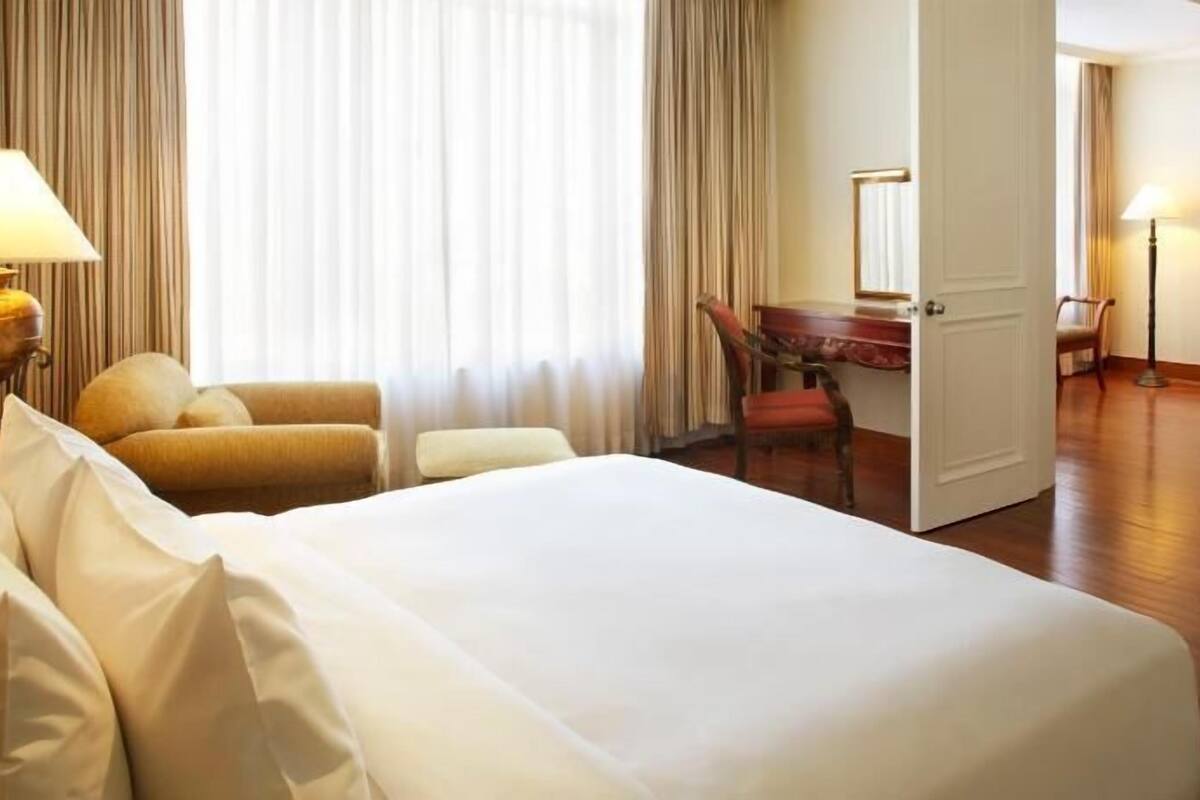 A hotel room with a bed, two armchairs, a desk, and a door leading to another room.