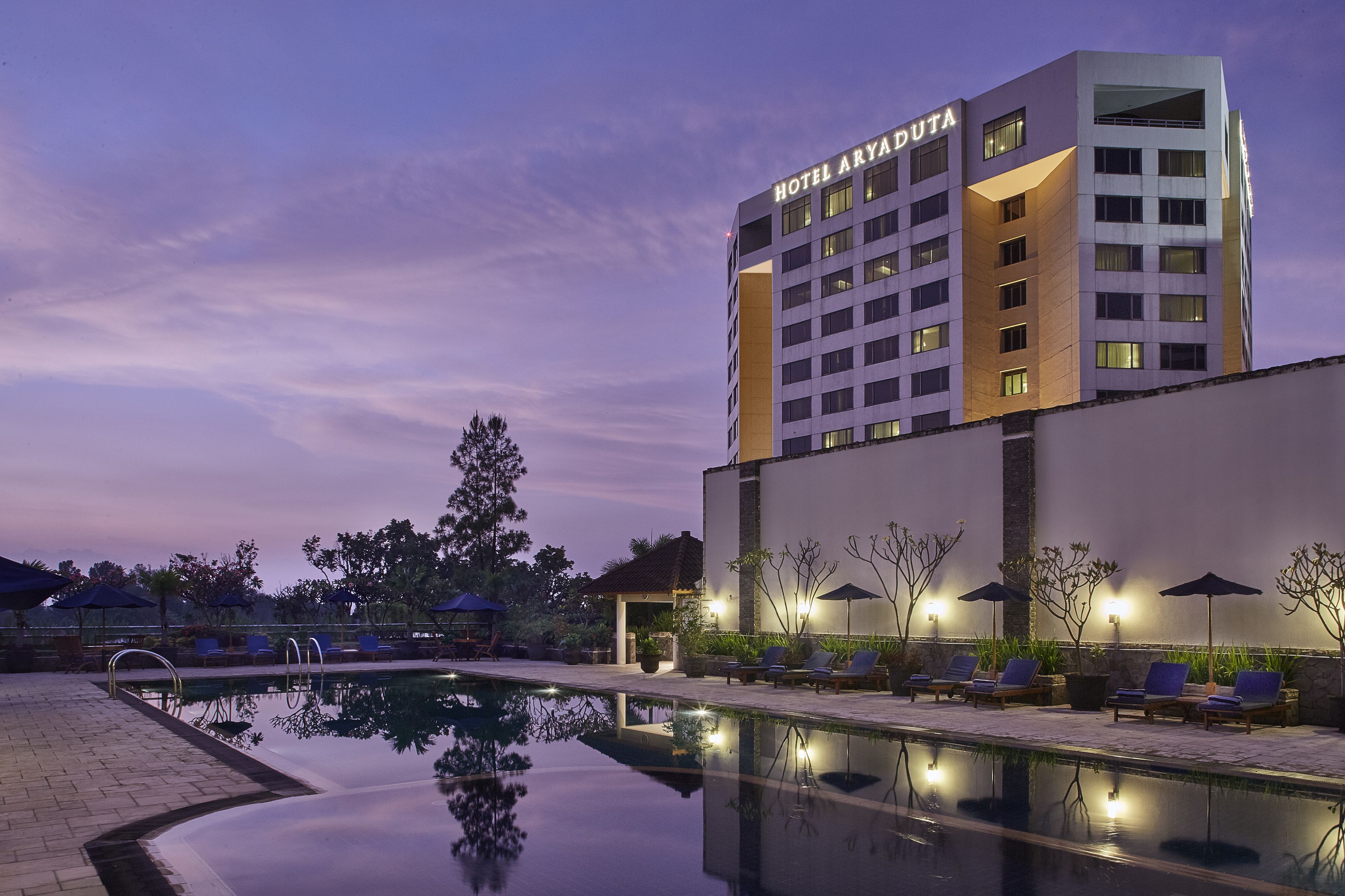 A hotel with a pool area, lounge chairs, and umbrellas.