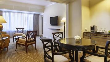 Habitación de hotel con comedor que incluye una mesa redonda, cuatro sillas, un televisor montado en la pared y una cafetera sobre una mesita.