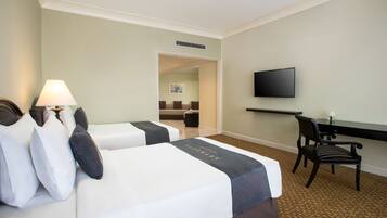 A hotel room with two beds, a desk, a chair, a TV, and a lamp.