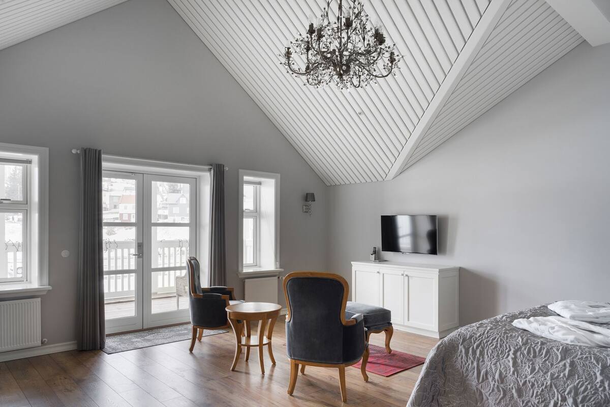 Camera da letto moderna con soffitto a falde, un lampadario, un letto, una televisione e vista panoramica attraverso una grande finestra.