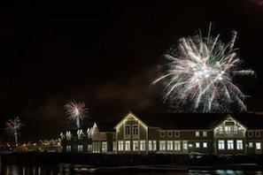 A waterfront hotel with illuminated windows and a view of fireworks in the background.