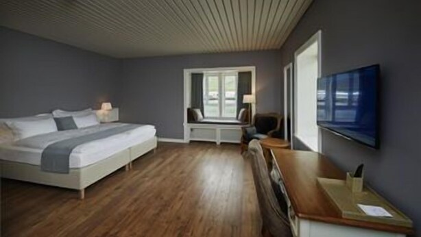Un dormitorio moderno con cama, escritorio, silla, televisor y ventana.