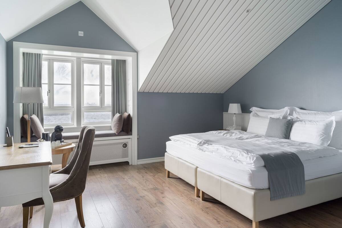 Una camera da letto con soffitto spiovente, un letto grande, una scrivania e una finestra con tende.