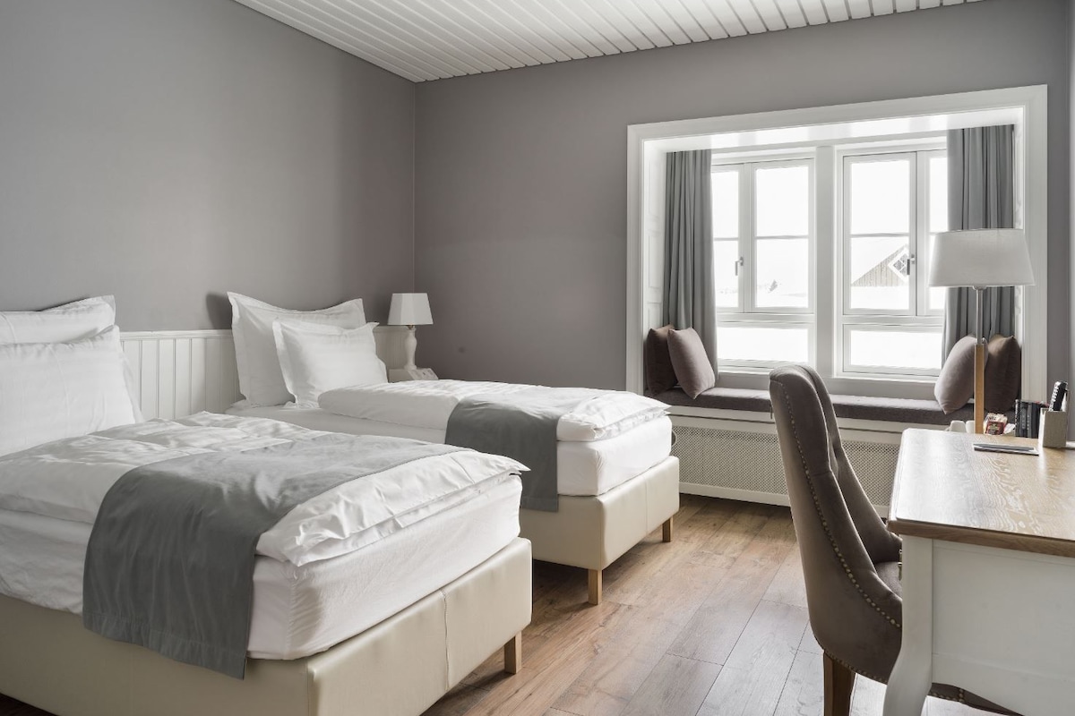 A hotel room with two beds, a desk, and a window with curtains.