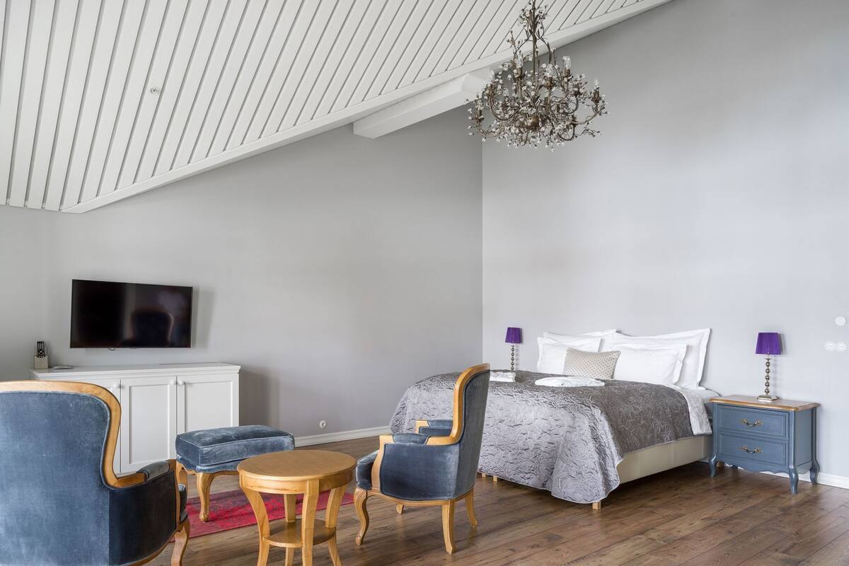 Una camera da letto moderna con un letto, due poltrone, un tavolino, una televisione e un lampadario.