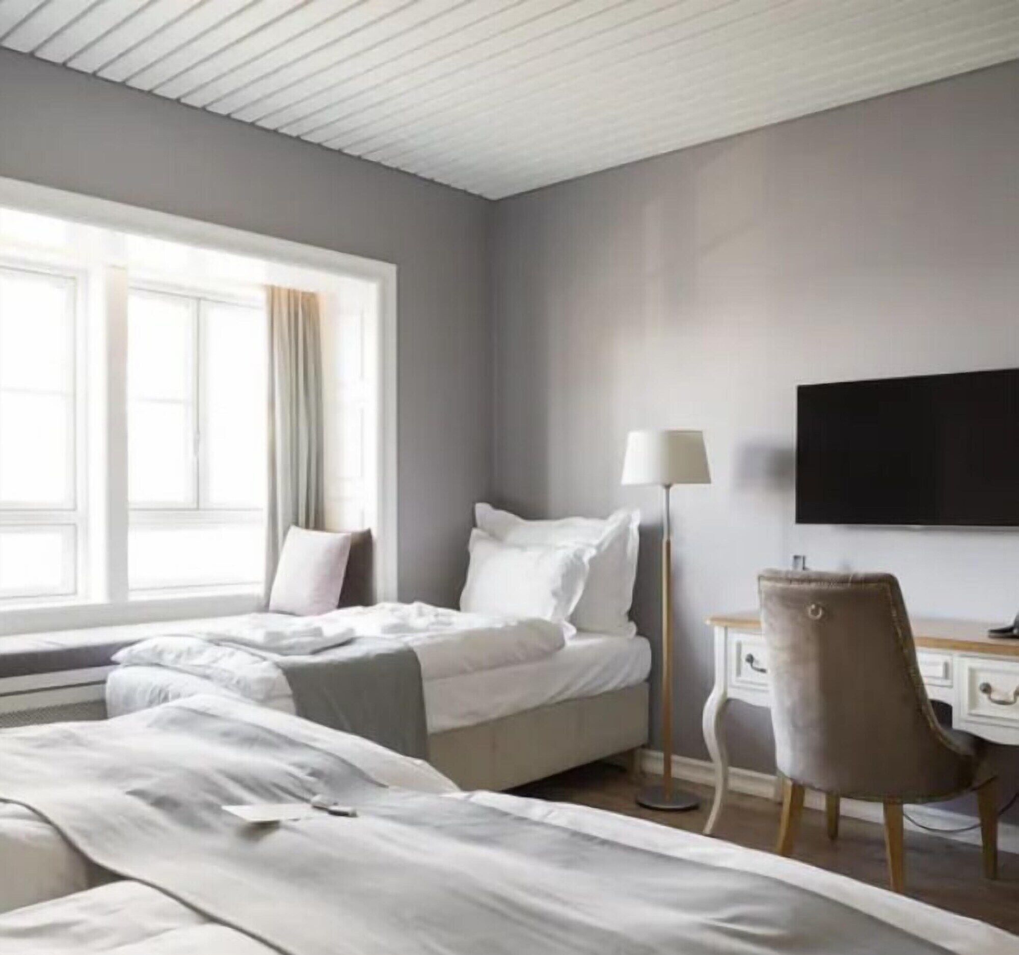 A hotel room with a bed, a desk, a chair, a TV, and a window with curtains.