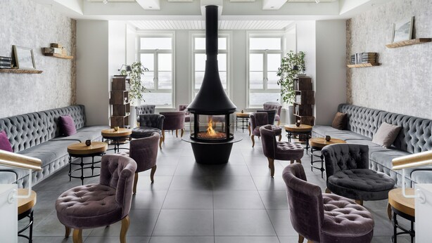 A modern interior with a fireplace, plush seating, and large windows. - Siglo Hotel (Siglufjordur)