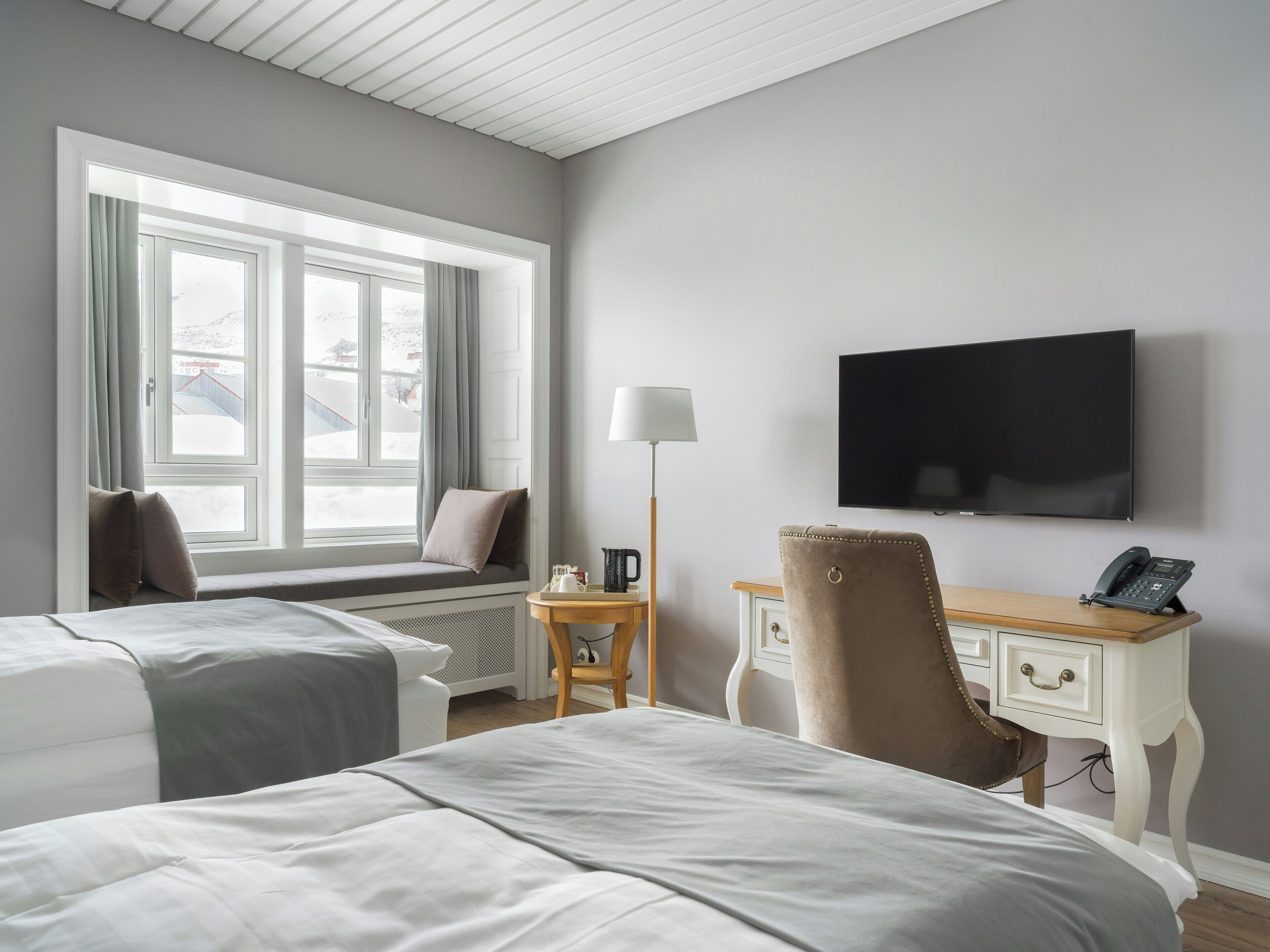 Habitación de hotel con dos camas, un escritorio con silla, un televisor y una ventana con cortinas.