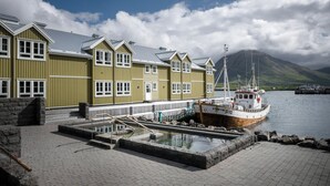 A row of green buildings with a dock and a boat. - Siglo Hotel (Siglufjordur)