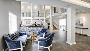 A spacious lobby with a high ceiling, a central seating area with blue upholstered chairs, a reception desk, and a staircase leading to an upper level. - Siglo Hotel (Siglufjordur)