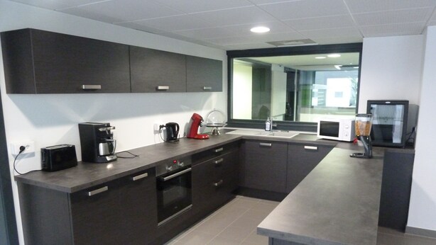 A modern kitchen with dark cabinetry, a built-in oven, a coffee maker, and a microwave. - Résidence Hôteliere Louise (Strasbourg)