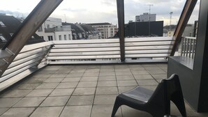 A rooftop terrace with tiled flooring, a metal railing, and a black plastic chair. - Résidence Hôteliere Louise (Strasbourg)