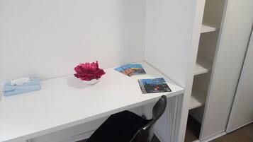Een wit bureau met een zwarte stoel, een zakdoos, een decoratieve bloem en een paar tijdschriften.