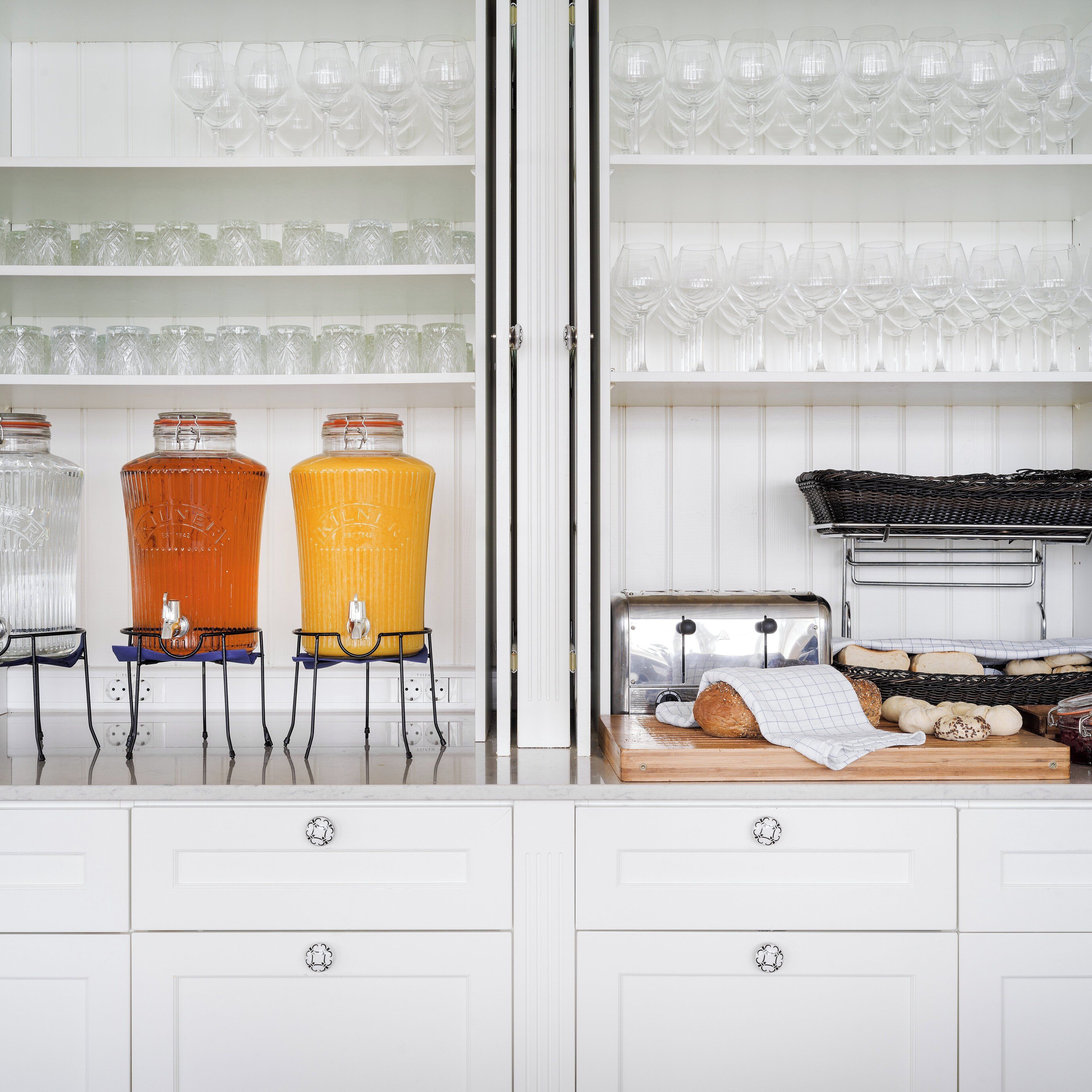 Una cocina con armarios blancos, una exhibición de pan y una bodega.