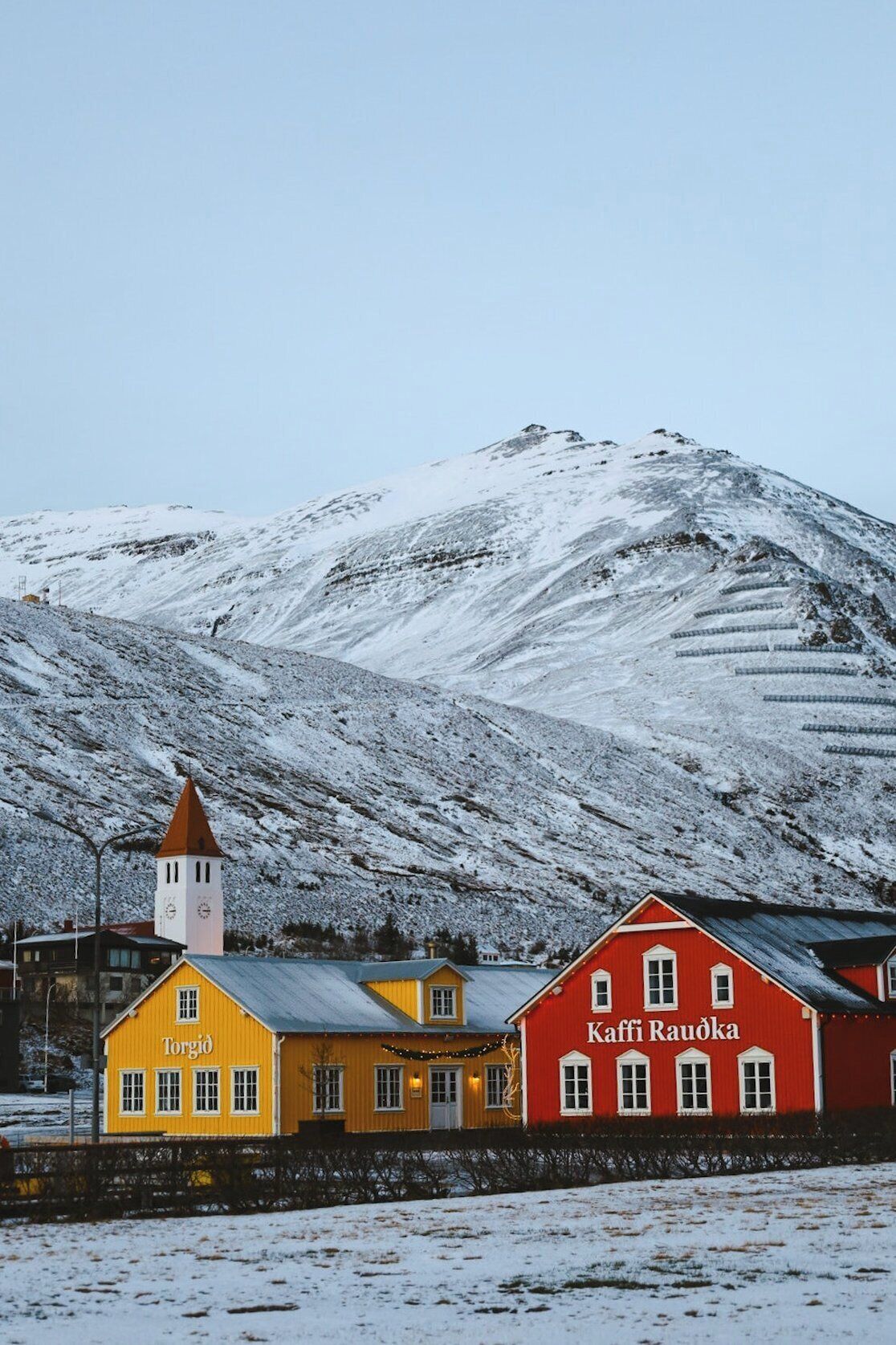 Montanha coberta de neve com uma igreja e dois edifícios, um amarelo e outro vermelho, em uma pequena cidade.