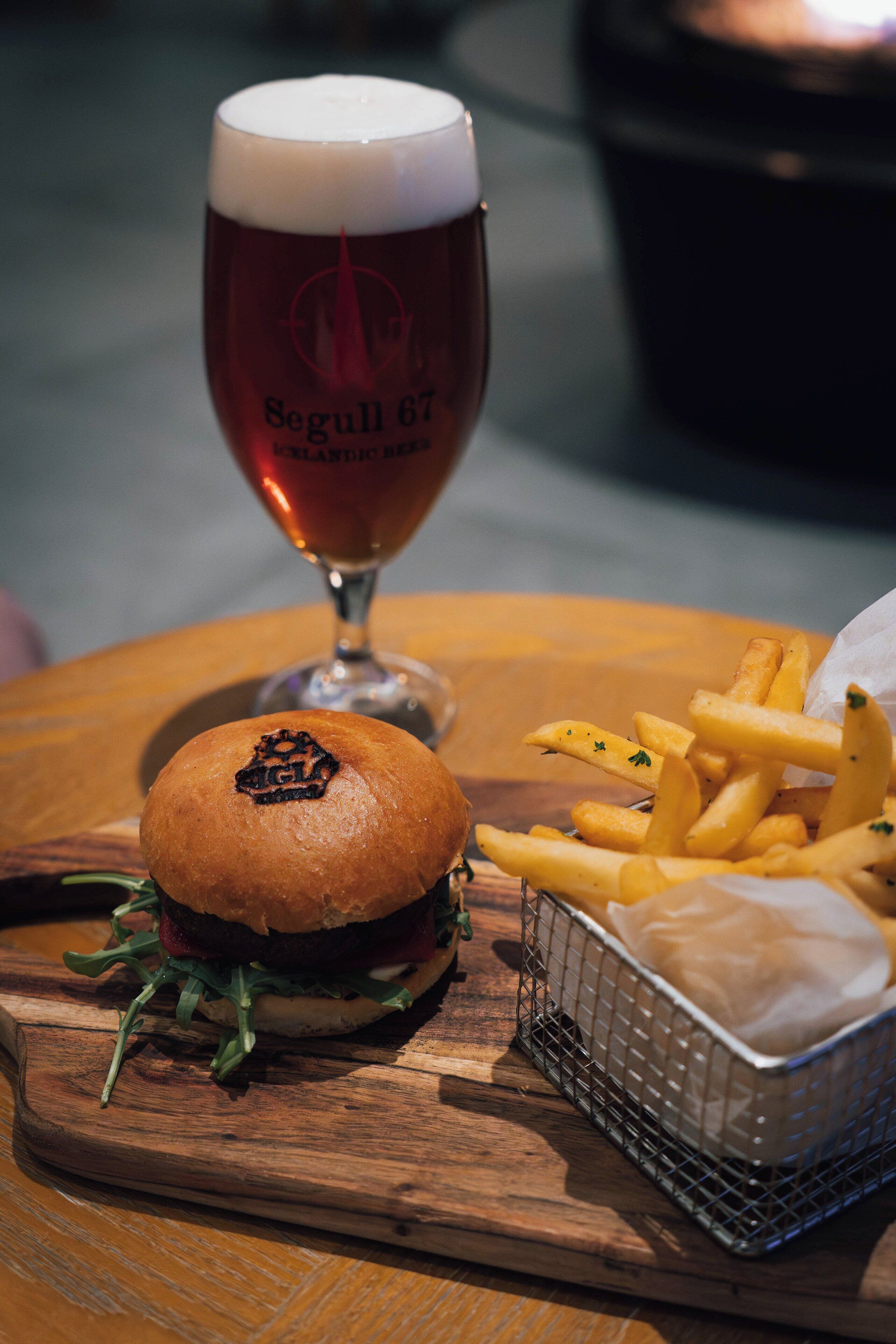 A burger, fries, and a glass of beer on a wooden table.