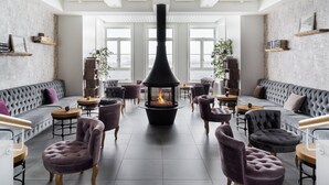 Un área de descanso moderna con chimenea central, disposición de asientos y amplios ventanales con vistas.