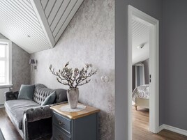 Un dormitorio con pared gris, cómoda de madera, sofá gris y un espejo grande.