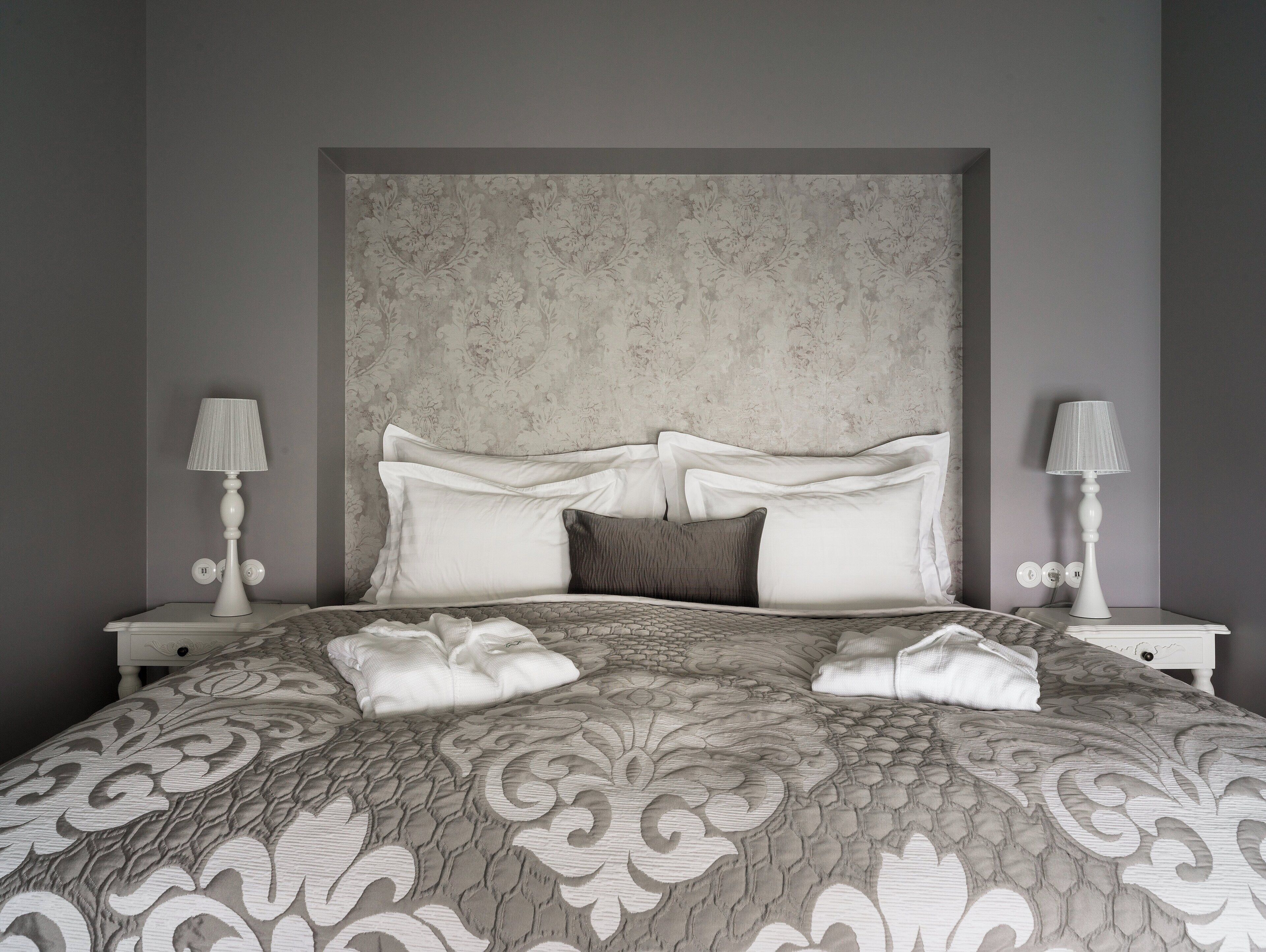 A neatly made bed with a patterned bedspread, two bedside lamps, and a headboard with a textured design.