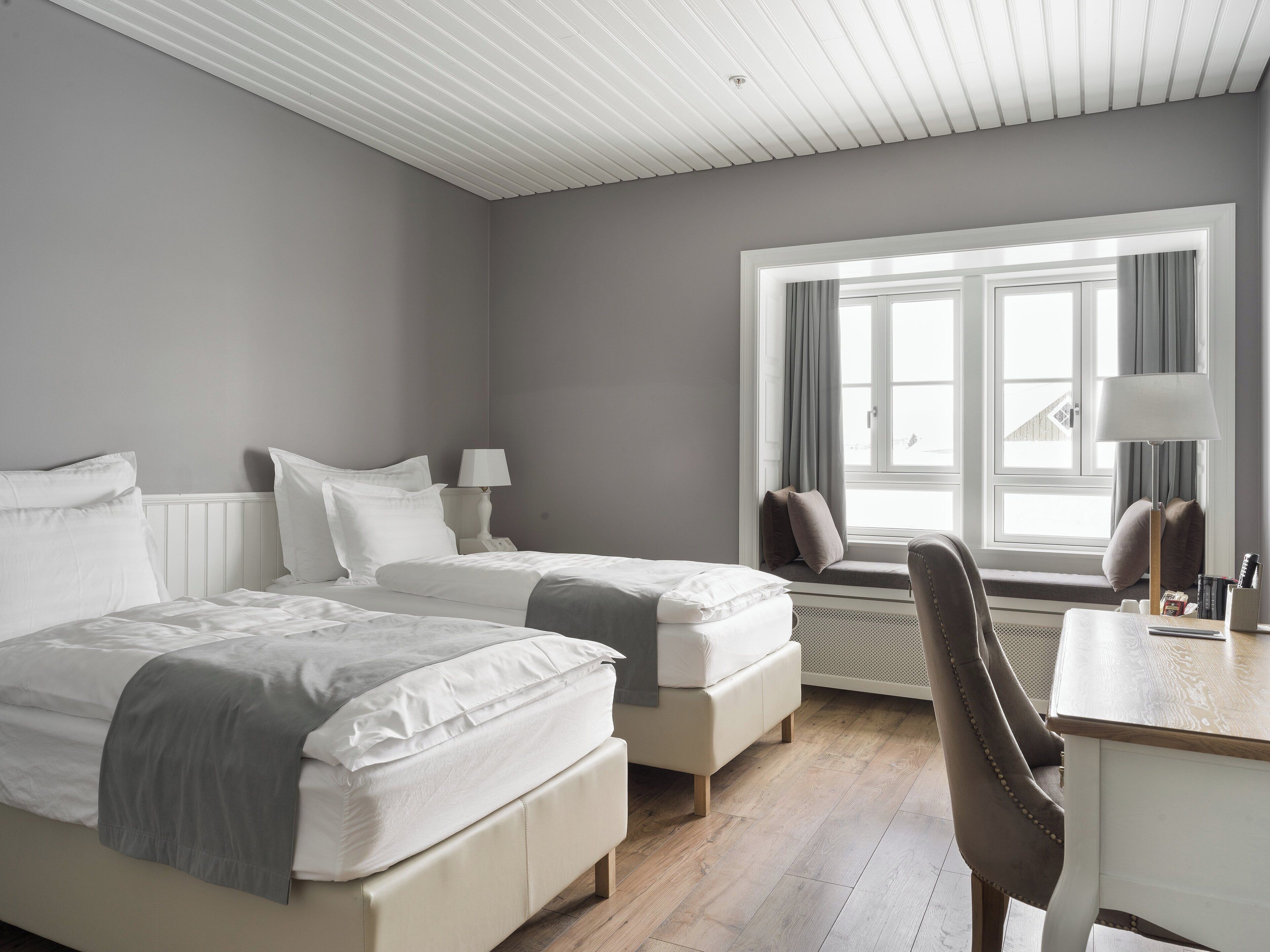 A hotel room with two beds, a desk, and a window with curtains.